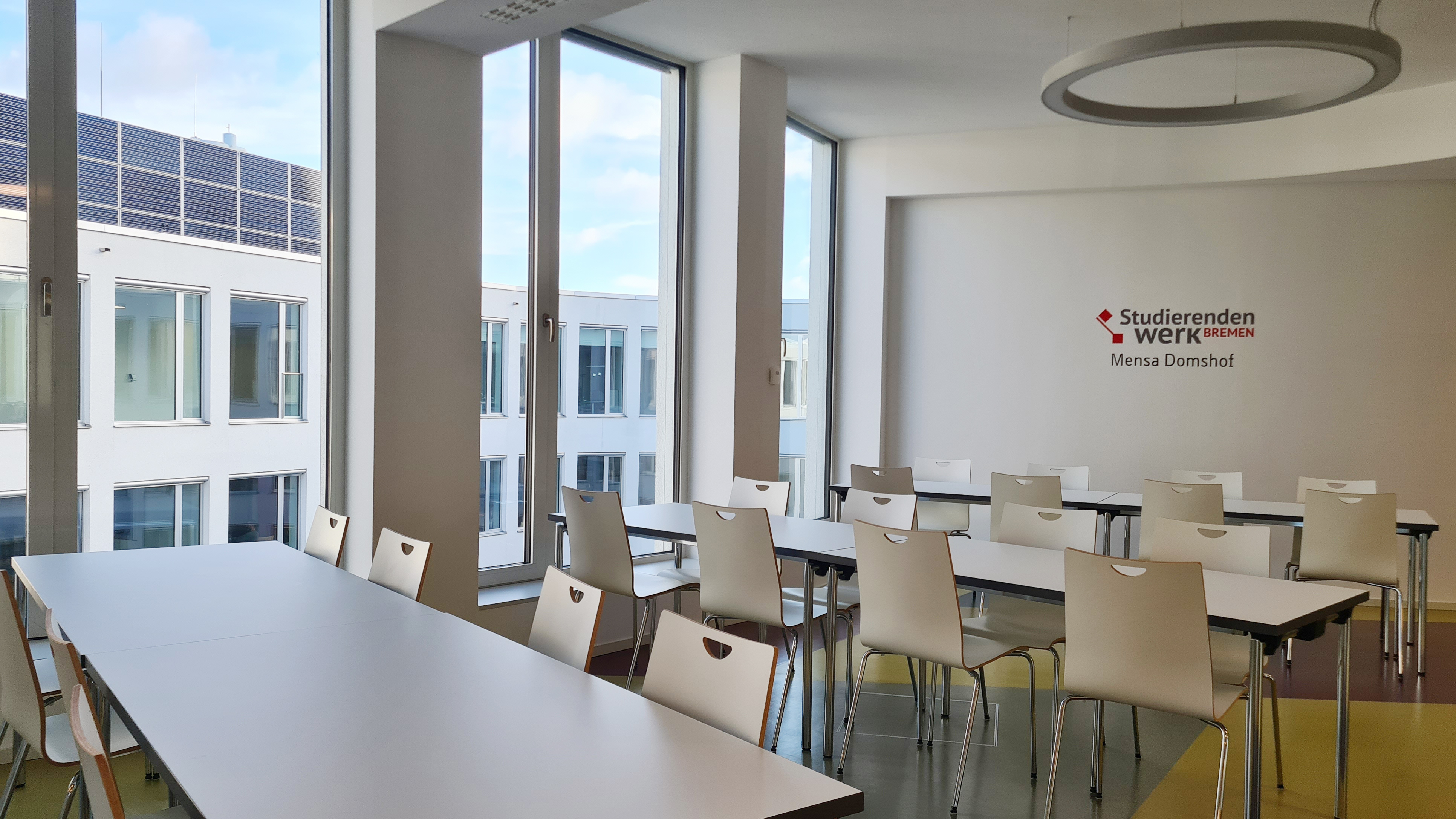 Sitzbereich mit Fenstern der Mensa Domshof mit dem Logo des Studierendenwerk Bremen an einer Wand.