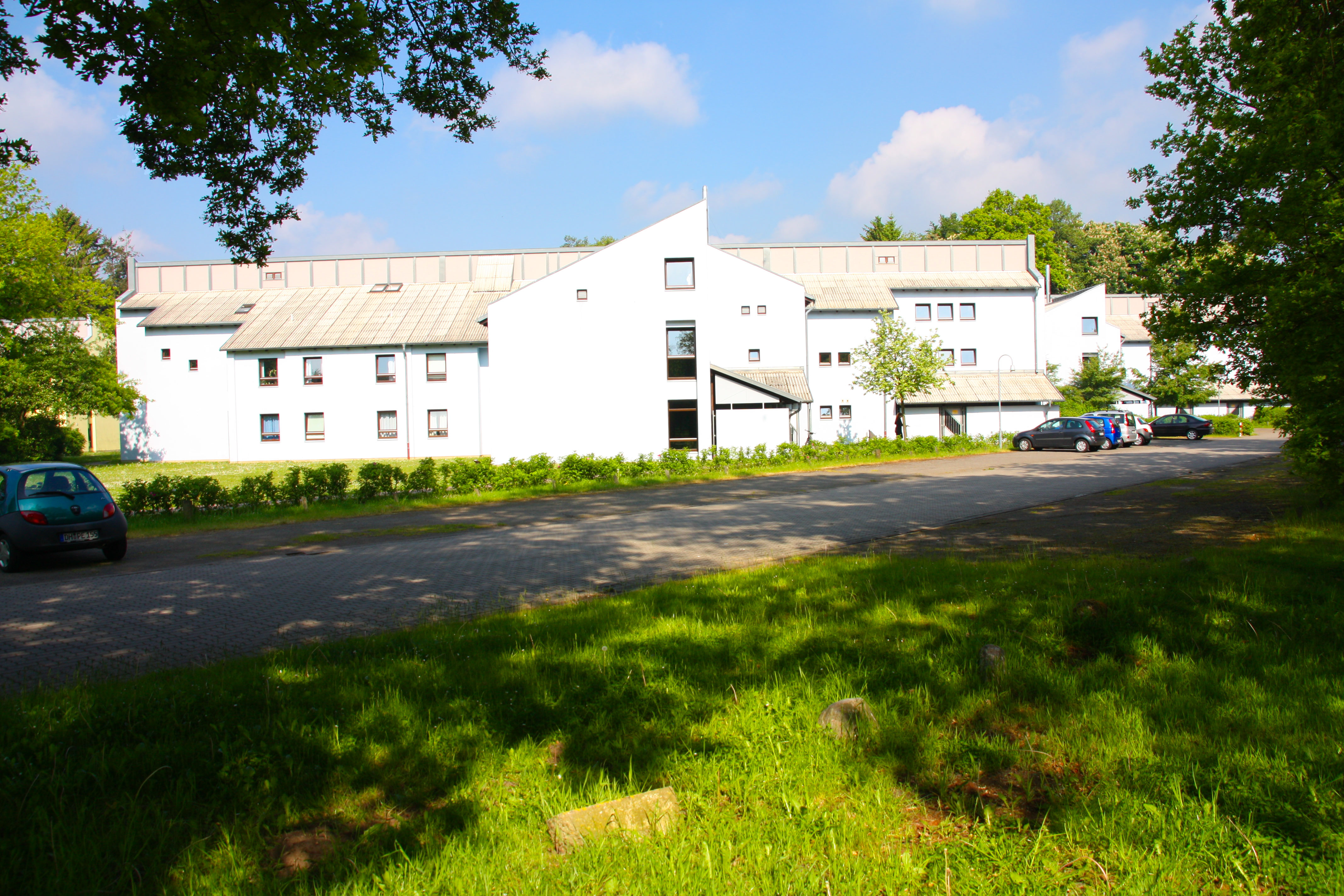 Außenansicht der Wohnanlage mit Wiese und Parkplatz davor.